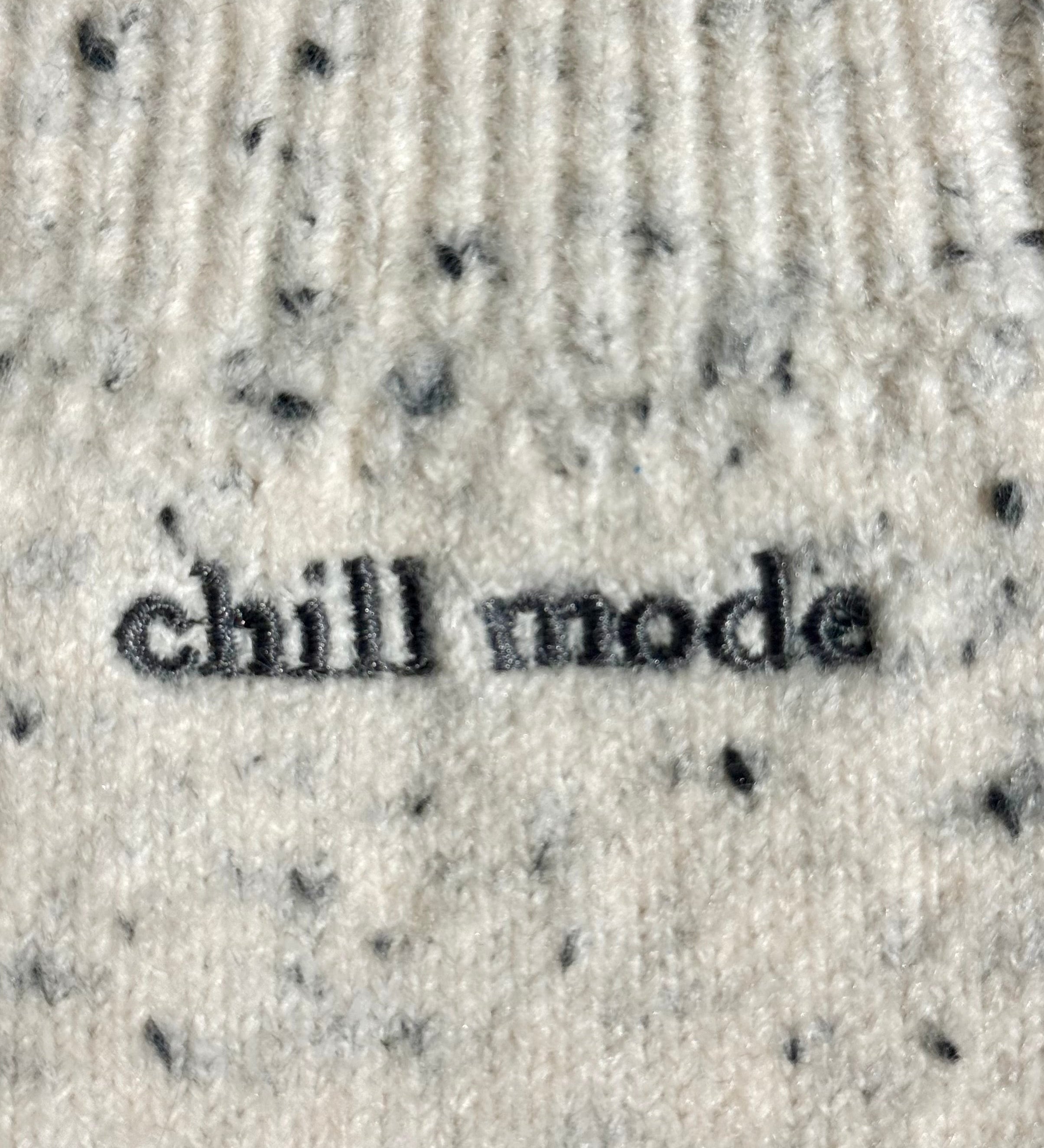Close-up of a ribbed knit sweater in a light cream color with small black speckles and the words 'chill mode' embroidered across the front.